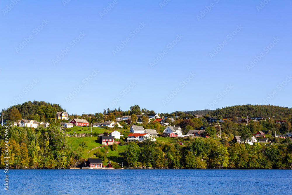 Colorful traditional Norwegian houses near the sea with green forest on mountains and blue sky