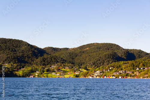 Colorful traditional Norwegian houses near the sea with green forest on mountains and blue sky