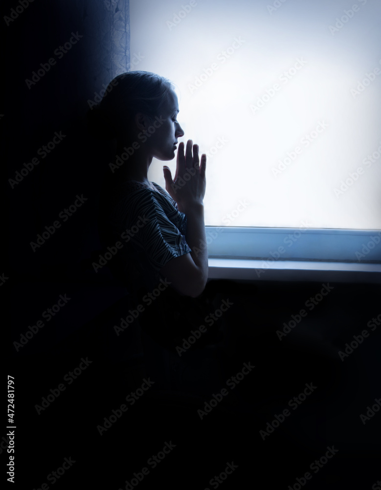 Young girl prays at the window
