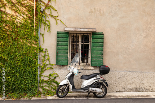 Typical Italian street scene with a white scooter by a window with green shutters on a tarmac street in Colognola ai Colli  Verona  Italy.