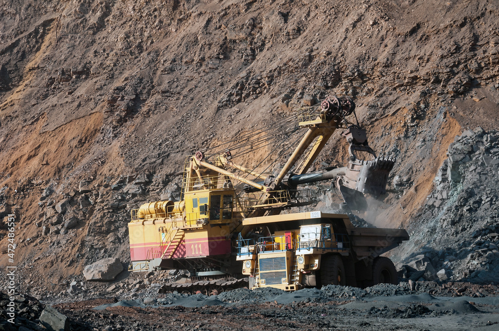 Quarry excavator loading iron ore into the heavy dump truck in iron ore open cast mine Quarry excavator loading iron ore into the heavy dump truck in iron ore open cast mine