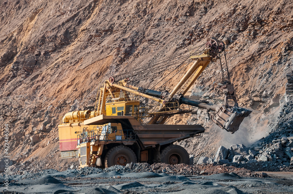 Quarry excavator loading iron ore into the heavy dump truck in iron ore open cast mine