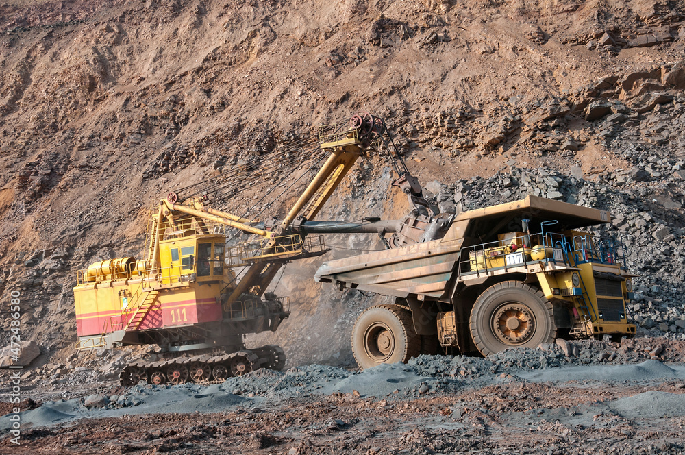 Quarry excavator loading iron ore into the heavy dump truck in iron ore open cast mine Quarry excavator loading iron ore into the heavy dump truck in iron ore open cast mine