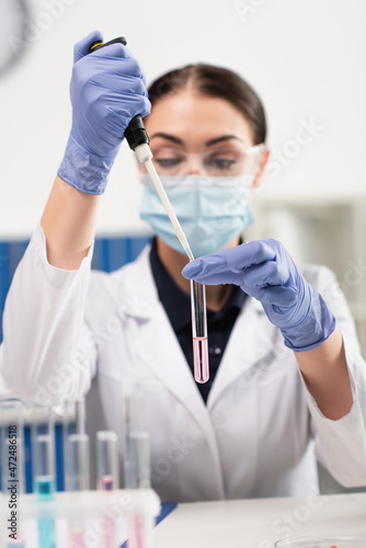 Scientist in latex gloves holding electronic pipette and test tube in laboratory.
