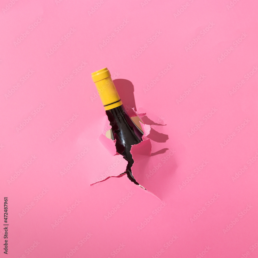 Champagne bottle tearing out of pink background. Minimal party concept
