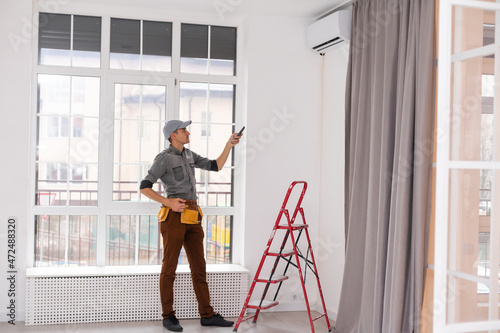 Young Man Repairing Air Conditioner Standing On Stepladder