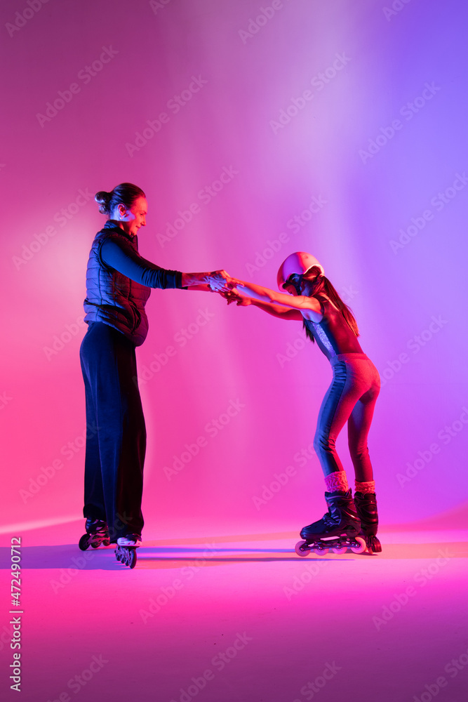 Fototapeta premium child skater athlete holding hands of her trainer, training for competition, photo on pink background in a studio 