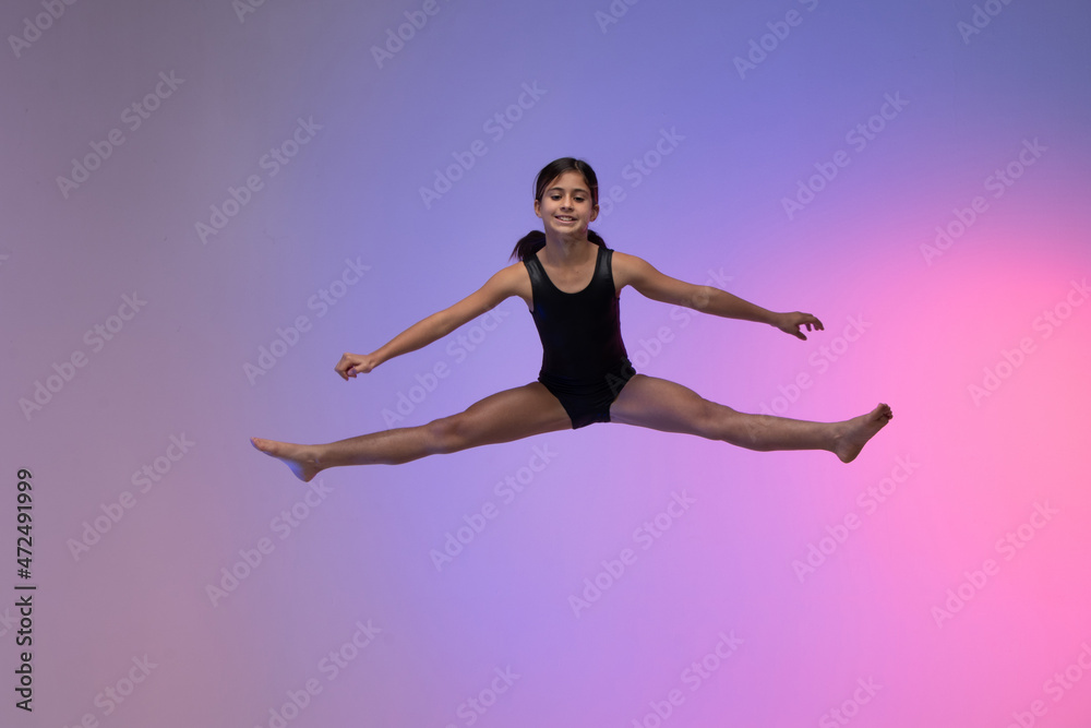 young gymnast athlete performing acrobatic jumps, training for competition, looking at photo, colorful background in a studio