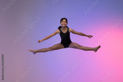 young gymnast athlete performing acrobatic jumps, training for competition, looking at photo, colorful background in a studio