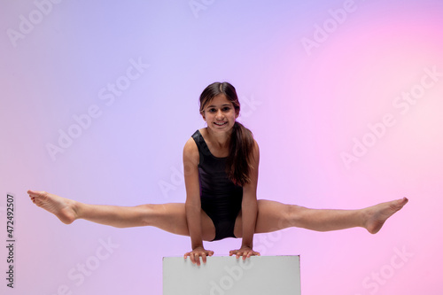 child athlete gymnast performing gymnastic exercise on top of apparatus, training for competition, colored background in a studio