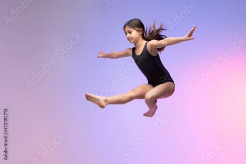 young gymnast athlete performing jumps, training for competition, colorful background in a studio.