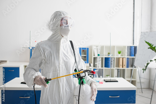 doctor in hazmat suit holding sprayer while making disinfection of laboratory.