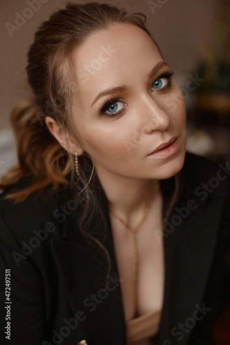 A fashionable young woman with perfect trendy makeup in an elegant suit posing in the interior. Charming model girl with seductive lips and deep blue eyes