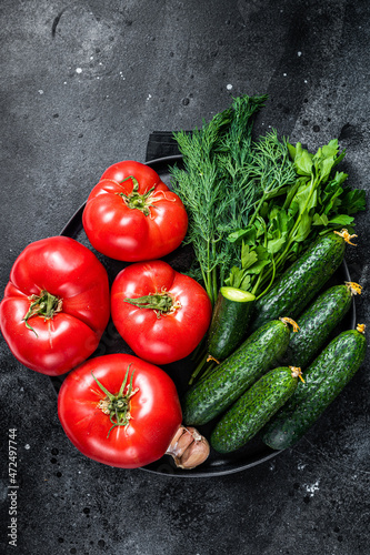 Fresh vegetables for summer green salad  red tomatoes  cucumbers  parsley  herbs. Black background. Top view