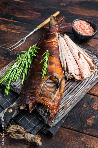 Cut Hot smoked fish  on a wooden board with rosemary. Dark wooden background. Top view