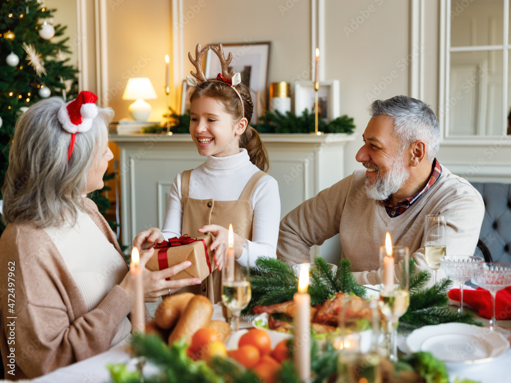 Little girl granddaughter giving Christmas gift to surprise grandmother during Xmas family dinner Little girl granddaughter giving Christmas gift to surprise grandmother during Xmas family dinner