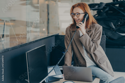 Woman in spectacles talking on phone while sitting at her workplace in office photo