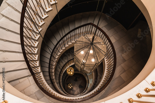Photo from above of a spiral staircase with three large lamps in shades of gold and brown.