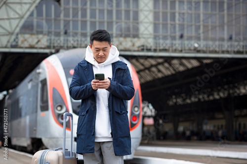 Asian tourist booking accommodation at home using mobile phone, passenger arrives by train to new city