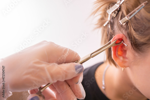 Professional placing the jewel of piercing on the ear with ball. Tragus type.