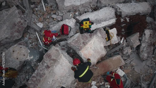 Zoom out drone view of rescuers and paramedics examining concrete debris of demolished building after earthquake photo