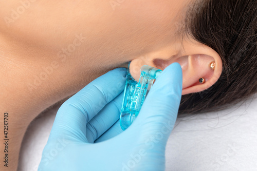Φωτογραφία A beautician makes a puncture of the earlobe with a disposable device in a beauty salon