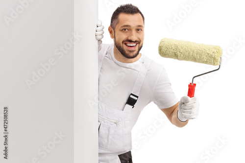 Fototapeta Naklejka Na Ścianę i Meble -  Painter holding a paint roller and looking at camera from behind a wall