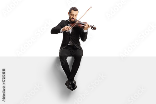 Full length shot of a violinist sitting on a blank panel and playing a violin photo