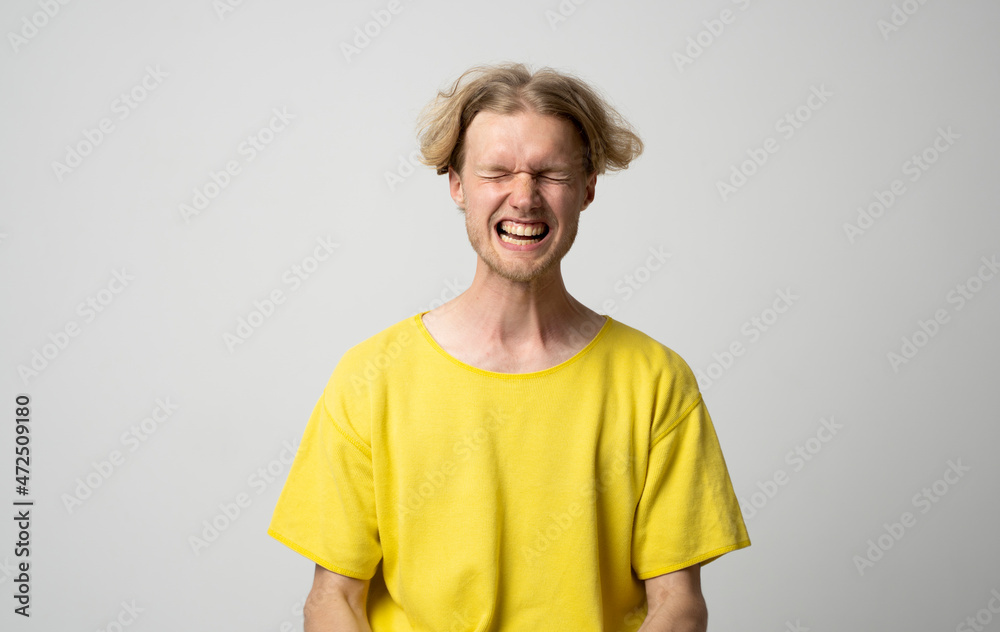 The young man in a yellow t-shirt is shouts isolated on white background. Angry. Screaming. Bad mood.