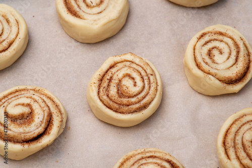 Raw cinnamon buns on baking paper ready for baking in the oven. Cooking tasty buns with cinnamon powder