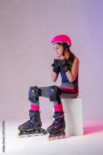 young skater athlete with pink helmet, adjusting protective gear, sitting, resting, training for competition, in a studio.