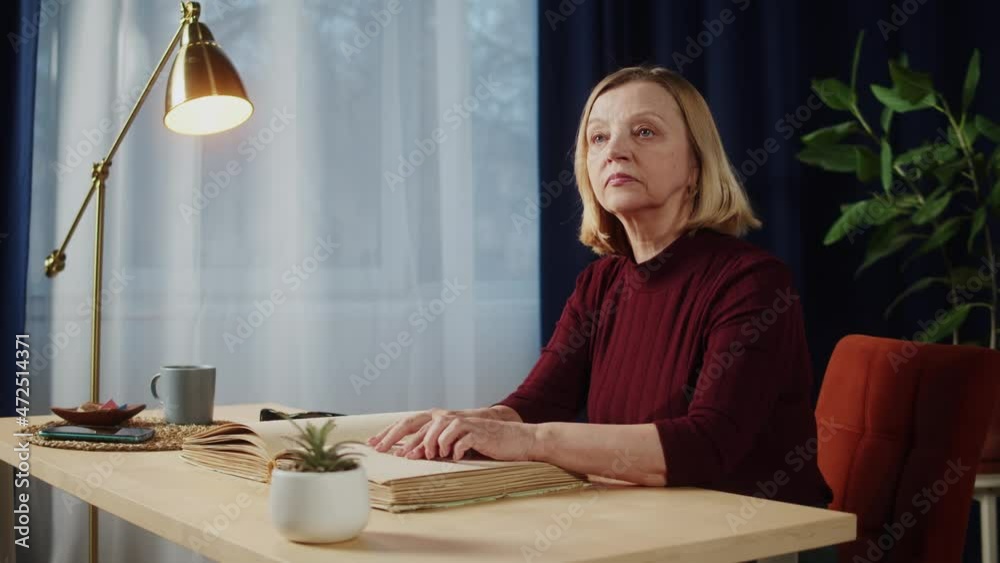Blind woman reading braille book using fingers, sitting in living room, poorly seeing female person learning to read, home education for people with disabilities, touching letters on sheet of paper. Blind woman reading braille book using fingers, sitting in living room, poorly seeing female person learning to read, home education for people with disabilities, touching letters on sheet of paper.
