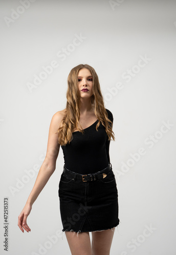 Beautiful young woman portrait in a black t-shirt and mini skirt. Studio shot, isolated on gray background.