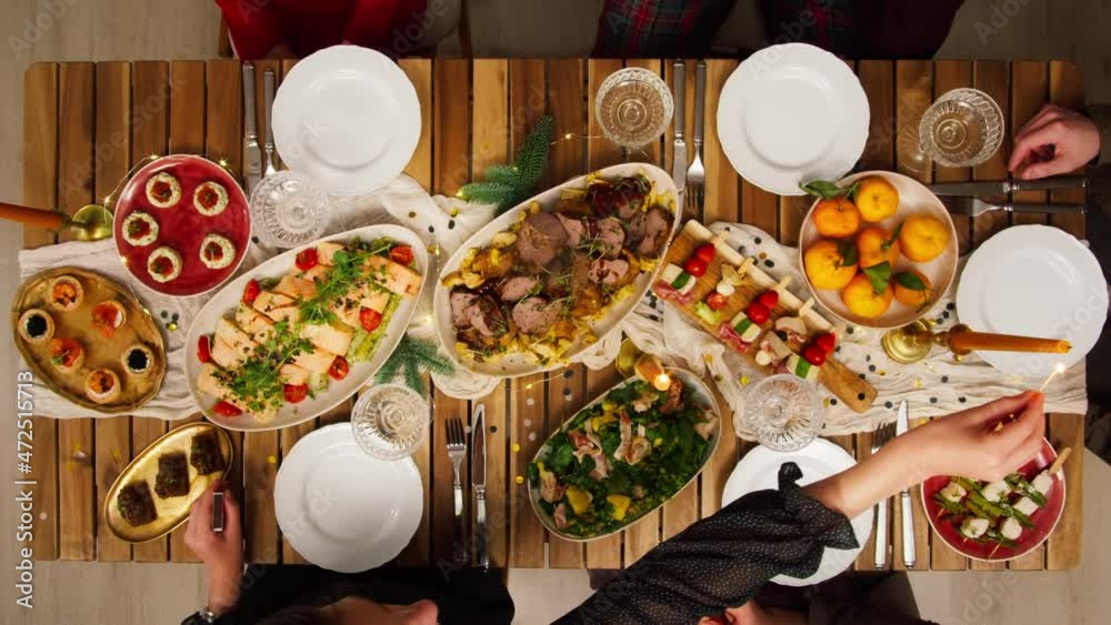 Friends celebrating new year top view, sitting at dining table. Young people drinking champagne and eating tasty food, toasting. Happy students during christmas party at home. 