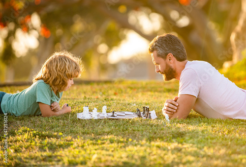 happy family of daddy and son boy playing chess on green grass in park outdoor, family