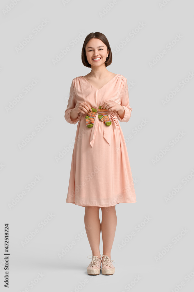 Young pregnant woman with baby socks on light background Young pregnant woman with baby socks on light background