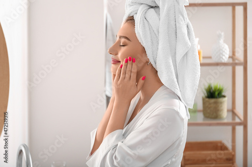 Pretty young woman applying facial cream in bathroom after shower