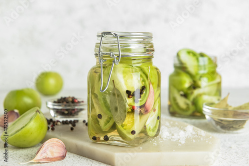 Jar with canned green tomatoes on light background