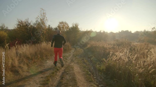 One bold young man running on dirt road holding a map in hand wearing black long sleaved thermal shirt. Spikelets field on the foreground. Copy space photo