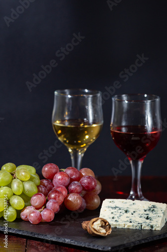 Wine, cheese, some grapes and pear on wooden plate on black background