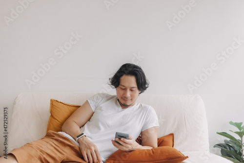 Freelance long hair Asian man sit on the sofa and use application smartphone.