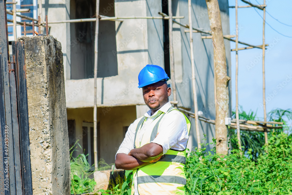 An African male construction worker on a building site, wearing a blue safety helmet and reflective jacket