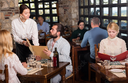 Charming young waiter receiving order from guests in country restaurant. High quality photo