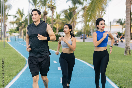 Group of three hispanic young adults running at a public path. Front view