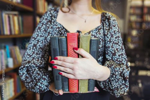 Girl is studying a book next to the rows of bookshelves.