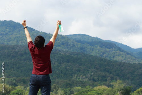 Happy man on redshirt take off medical face mask, raise and open arms, take a deep breath of fresh air in the park.new normal safe life escapes step, Relaxation during Covid-19 concept.