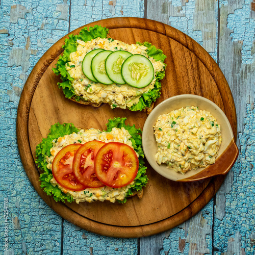 Homemade egg salad sandwich with wholewheat bun,cucumber, tomatoes,lettuce,egg,and cream cheese.  Rustic style. Selective Focus. Top view. Copy space. No.017