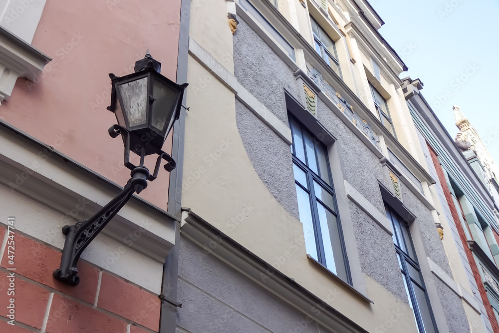Tallinn, Estonia, Europe - 26 Nov 2021: Close up, selective focus of old-style black street lamp lantern on the renewed pink, grey, and yellow building facade wall with window. Vanalinn. Tallinn, Estonia, Europe - 26 Nov 2021: Close up, selective focus of old-style black street lamp lantern on the renewed pink, grey, and yellow building facade wall with window. Vanalinn.