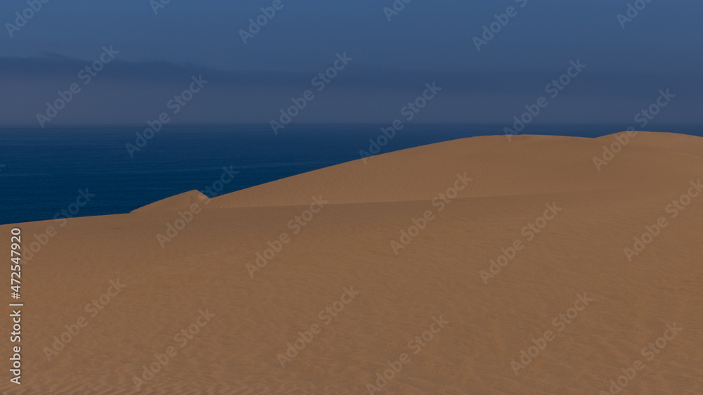 Eine grosse Sanddüne vor dem blauen Atlantik, über dem Dunst aufsteigt