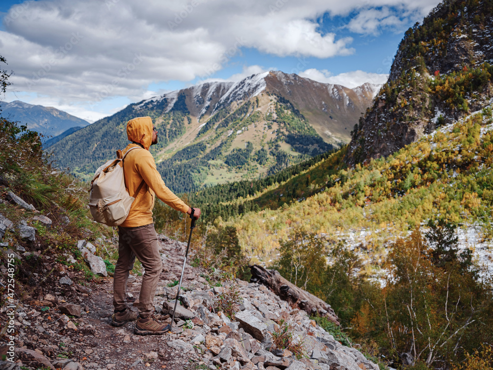 Fototapeta premium travel to Caucasus mountains in Karachay-Cherkessia, Arkhyz. Man in yellow hipster hoodie hiking in mountains with travel backpack. Wandering lifestyle, adventure concept autumn vacation in wild